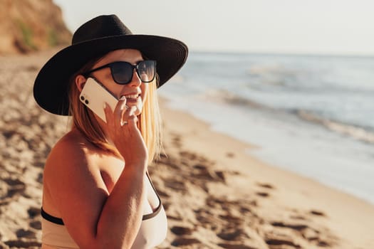 Close Up of Smiling Young Woman in Sunglasses and Hat Looking Towards the Sea While Talking on the Phone