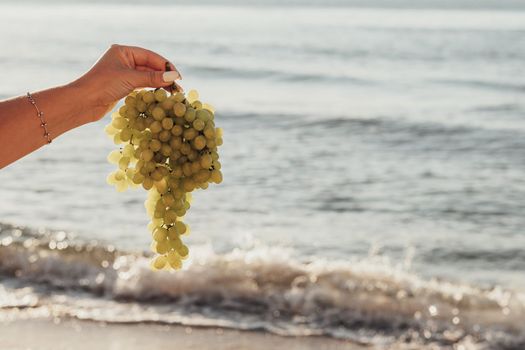 Female Hand Holding Branch of Grapes on Background of the Sea