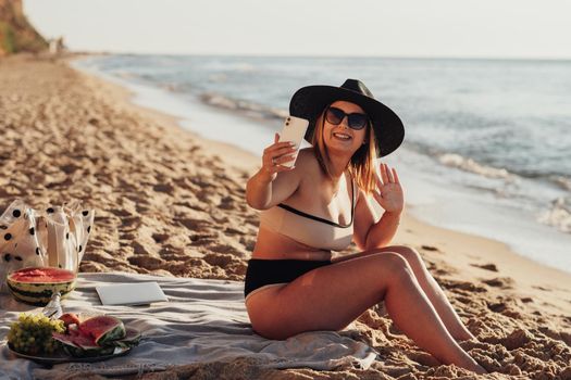 Smiling Young Woman Taking Video Call on the Phone While Sitting on Sandy Beach by Sea