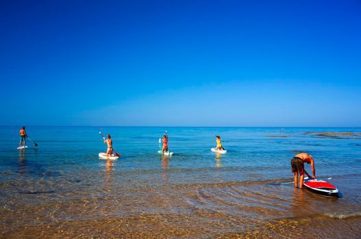 Realmonte, Italy - July 23,: Stand up paddle boarding. Joyful group of friendsare training SUP board in the mediterranean sea on a sunny morning in Realmonte beach on July 23, 2021