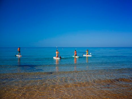 Realmonte, Italy - July 23,: Stand up paddle boarding. Joyful group of friendsare training SUP board in the mediterranean sea on a sunny morning in Realmonte beach on July 23, 2021