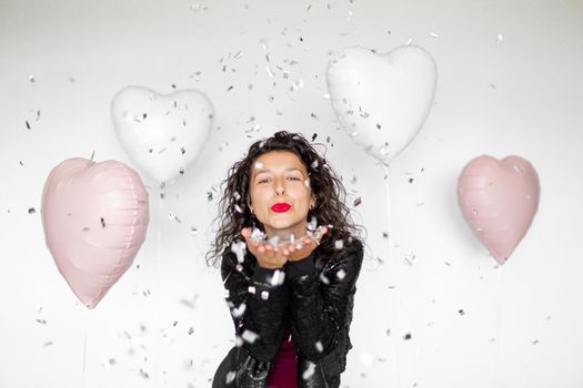 The emotion of success. Happy sexy brunette girl enjoying celebrating with confetti and heart balloons on a white background.