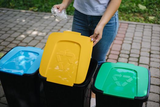 Female in the park throwing plastic bag into recycling bin. Different colours on plastic bins. Green, blue and yellow.