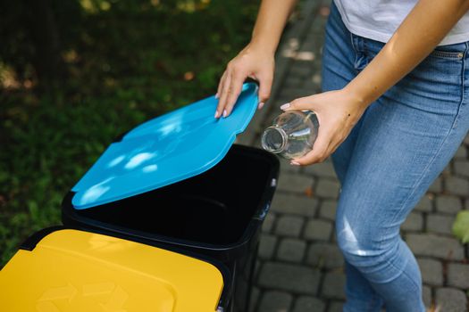 Closeup portrait woman hand throwig empty glass bottle in recycling bin. Different colour of plastic bins in the park.