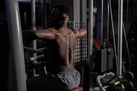 Shirtless african american man doing back exercises on a machine in the gym