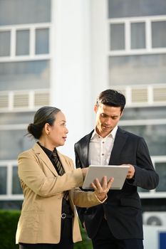 Elegant business people in formalwear talking while walking outdoors on street in modern city.