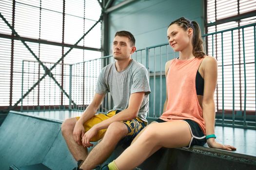 Young man and woman having fun on roller skates in skate park. Extreme sport competition. Indoors skate park equipment. Hobby