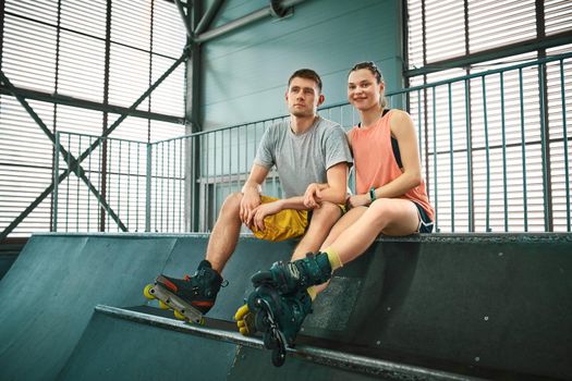 Young man and woman having fun on roller skates in skate park. Extreme sport competition. Indoors skate park equipment. Hobby