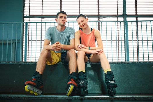 Young man and woman having fun on roller skates in skate park. Extreme sport competition. Indoors skate park equipment. Hobby