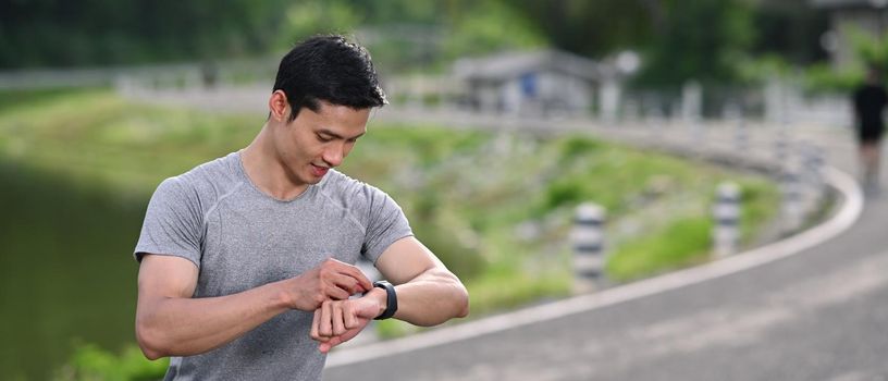Sport man checking his heart rate data on smartwatch during morning workout in the park.