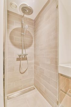 Shower faucets attached to tiled wall near glass partition and ornamental curtail in washroom at home