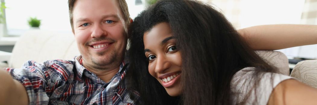 Portrait of friends taking selfie on sofa. Middle aged man and latinoamerican woman smiling for picture, warm friends meeting. Friendship, pastime, fun and happiness concept