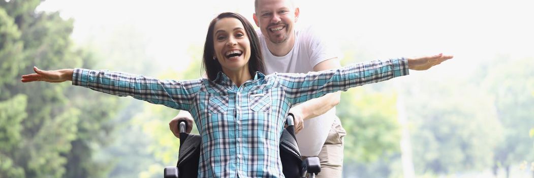 Portrait of cheerful woman sitting in wheelchair. Middle aged man pushing female in park and laughing. Fun, pastime, nature, relationship, love, quality time concept