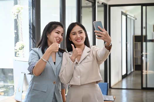 Two cheerful female business colleagues taking a selfie with smart phone at office.