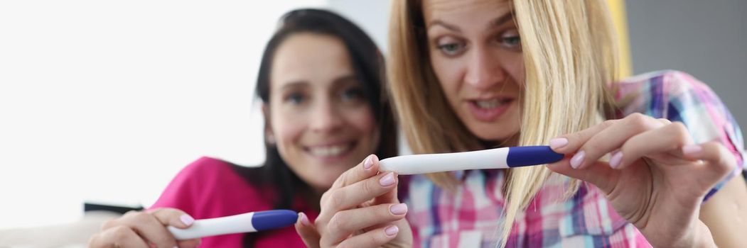 Portrait of best friends look at pregnancy test results, positive result on tools. Both pregnant, share happiness, waiting for new life. Baby, pregnancy, family, friendship concept. Blurred background