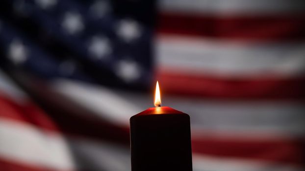 Burning candle against the background of the waving flag of the united states of america in the dark