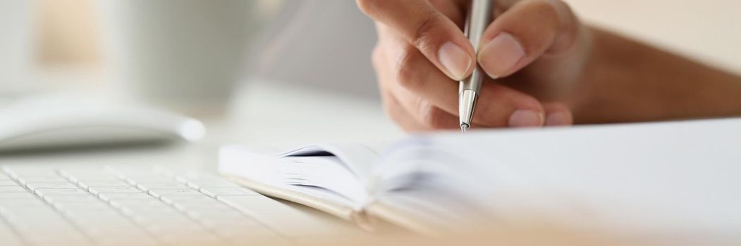 Close-up of person writing down ideas, impressions, making notes for future, planning day. Hand holding silver pen. Journaling, creativity, writer, thoughts concept. Blurred background