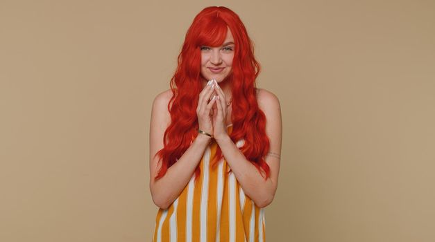Sneaky cunning woman with tricky face gesticulating and scheming evil plan, thinking over devious villain idea, cunning cheats, jokes and pranks. Redhead girl on beige studio background alone indoors