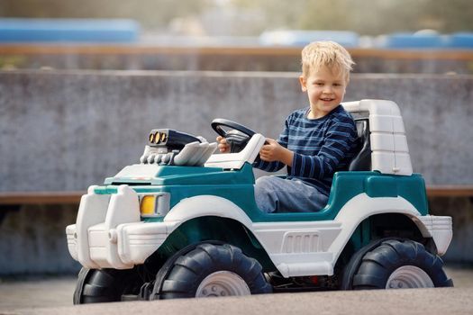 Happy little boy driving big toy car and having fun, outdoors.