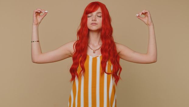 Keep calm down, relax, inner balance. Woman breathes deeply with mudra gesture, eyes closed meditating with concentrated thoughts, peaceful mind. Redhead adult girl isolated on beige studio background