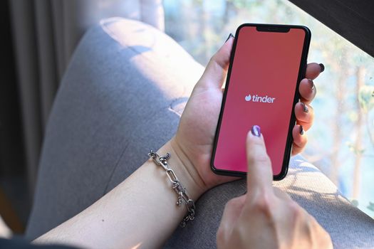 Chiang Mai, Thailand - Mar 01,2022: Woman holding smart phone with Tinder app on screen. Tinder is a location based dating and social discovery service application.