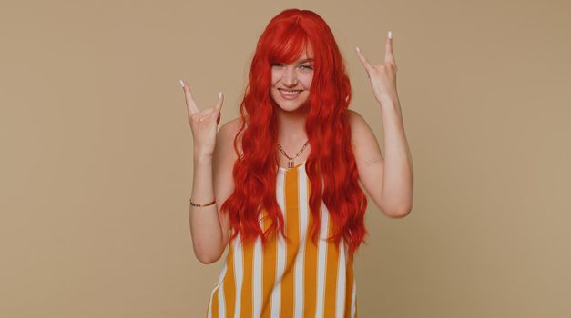Rock n roll. Overjoyed delighted redhead woman in tank top showing gesture by hands, cool sign, shouting yeah with crazy expression, dancing, emotionally rejoicing in success win alone on beige wall