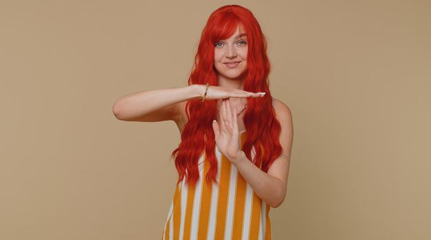 Tired serious upset ginger woman in tank top showing time out gesture, limit, stop break sign, no pressure, I need more time. Young adult redhead girl isolated alone on beige studio wall background