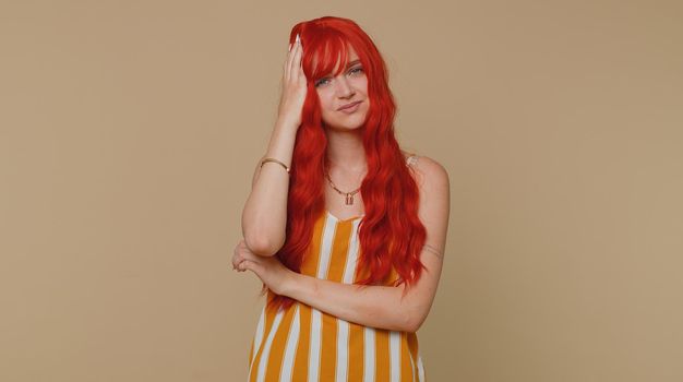 Red hair young woman in tank top rubbing temples to cure headache problem, suffering from tension and migaine, stress, grimacing in pain, high blood pressure. Girl isolated alone on beige background