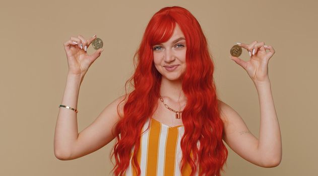 Redhead woman winner showing golden bitcoins. Career wealth cryptocurrency investment mining future technology. Young ginger girl fooling making faces. Happy businesswoman isolated on beige background