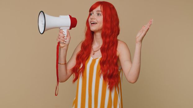 Smiling happy redhead woman talking with megaphone, proclaiming news, loudly announcing sale advertisement, warning using loudspeaker to shout speech. Young ginger girl on beige studio background