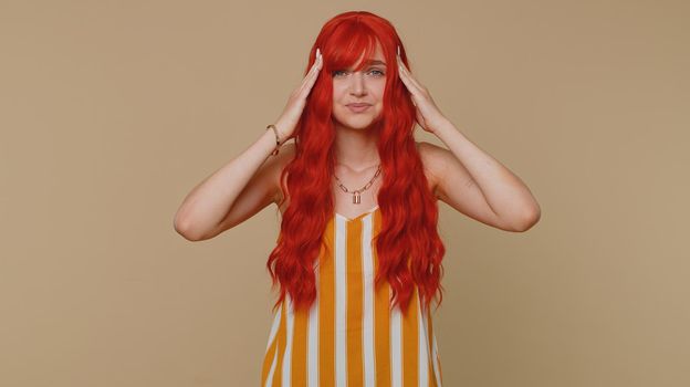 Redhead young woman in tank top rubbing temples to cure headache problem, suffering from tension and migaine, stress, grimacing in pain, high blood pressure. Girl isolated alone on beige background