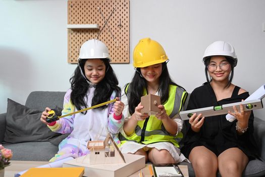 Three lovely asian girls wearing safety helmet pretend to be engineer while playing together at home.