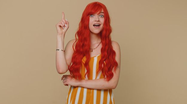 Eureka. Inspired ginger woman in tank top pointing finger up with open mouth, showing Eureka solution idea gesture, inspiration, answer. Young adult girl isolated alone on beige studio wall background