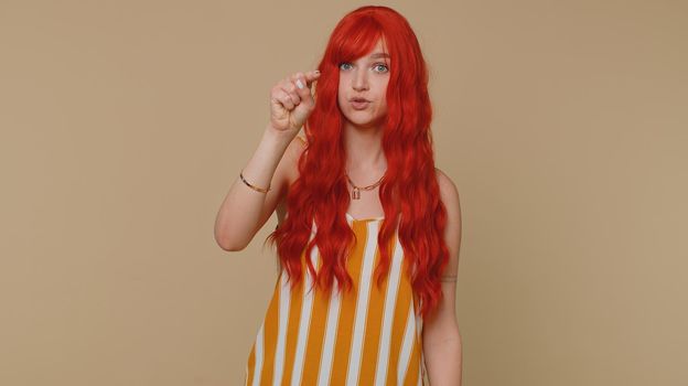 Hey you. Ginger woman in tank top smiling excitedly and pointing to camera, choosing lucky lottery winner, indicating to awesome you. Young redhead girl isolated alone on beige studio wall background