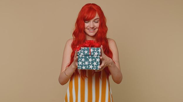 Cheerful red hair young winner woman receive gift box, birthday surprise and expressing great happiness amazement, satisfied with best present bonus. Ginger girl isolated on beige studio background