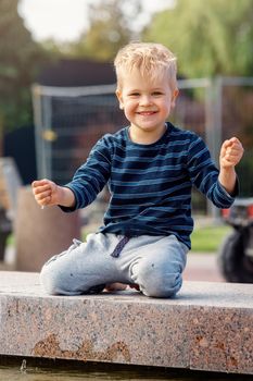 A little funny boy climbed on a parapet of a fountain and touch the water.