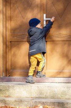 Little boy try to reach handle of big brown door.