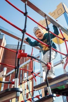 Little smiling boy trains and bravely crosses the rope bridge.