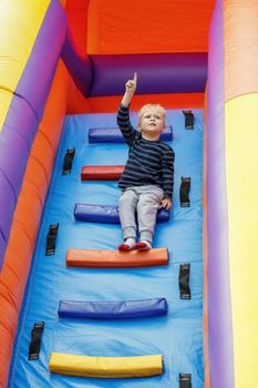 A brave little boy on top of an inflatable trampoline. The child points his finger at the sky, he sees the birds flying.