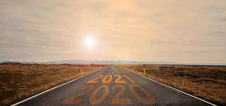 The word 2021 written on highway road in the middle of empty asphalt road at golden sunset and beautiful blue sky. High-quality photo