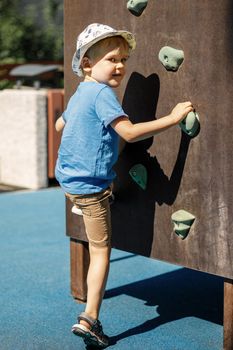 A young mountaineer trains to climb the climbing wall. Active child time spending concept image.