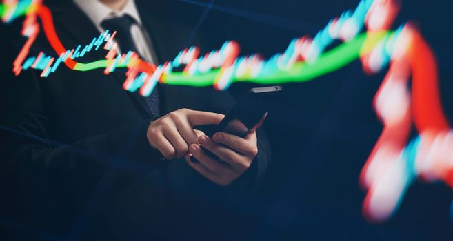 Man using smartphone with graphs analysis candle line and foreign currency rate on bokeh colors light. Manager analyzing investment statistics and indicators on dashboard for trading products.