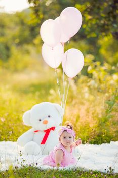 girl sitting in nature with teddy bear and balloons