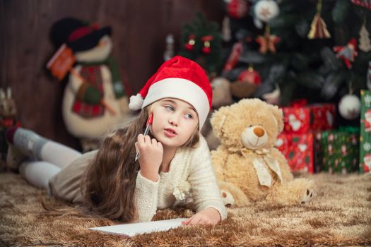 girl writing a letter to santa claus on the background of a decorated christmas tree