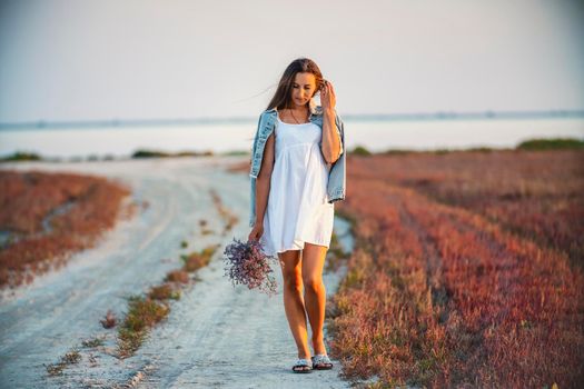 Woman with a bouquet of flowers walking on the road against the background of the sea