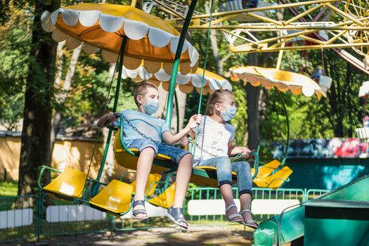 children wearing medical masks ride a carousel in the park