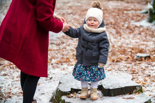 mom straightens daughter's jacket in the park in winter