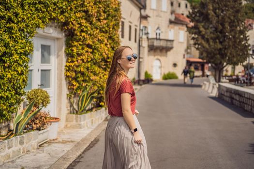 Woman tourist enjoying Colorful street in Old town of Perast on a sunny day, Montenegro. Travel to Montenegro concept. Scenic panorama view of the historic town of Perast at famous Bay of Kotor on a beautiful sunny day with blue sky and clouds in summer, Montenegro, southern Europe.