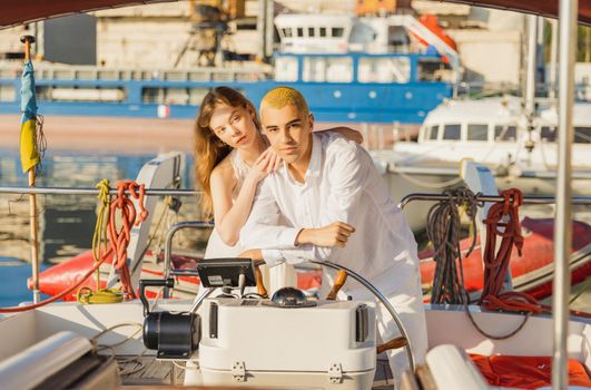 a couple in white clothes stands near the steering wheel on a yacht