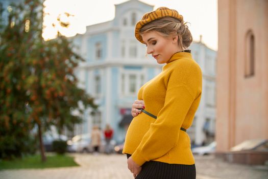 pregnant woman in a yellow sweater on the background of the city